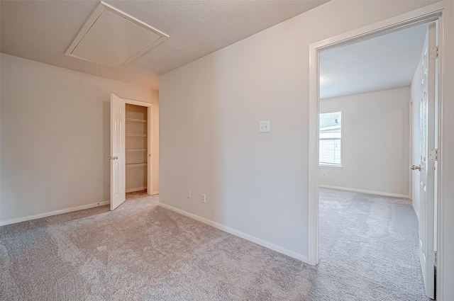 empty room featuring attic access, light colored carpet, and baseboards