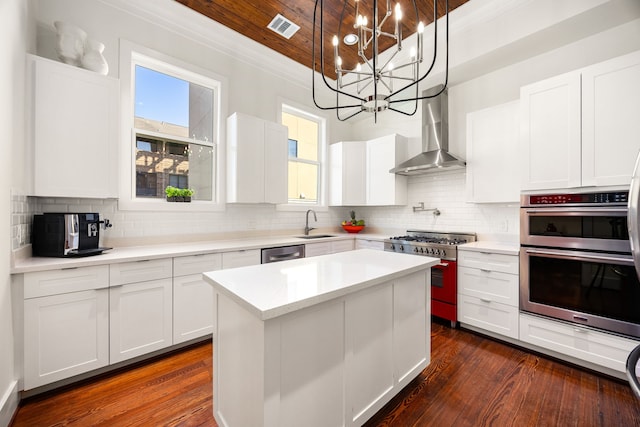 kitchen featuring visible vents, hanging light fixtures, appliances with stainless steel finishes, white cabinets, and wall chimney range hood