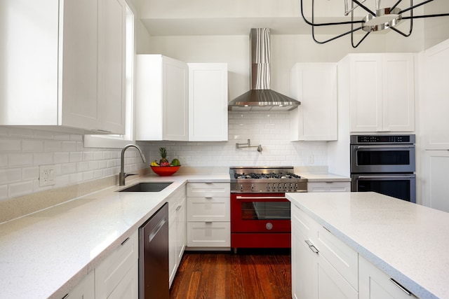 kitchen featuring stainless steel appliances, decorative backsplash, white cabinets, a sink, and wall chimney range hood