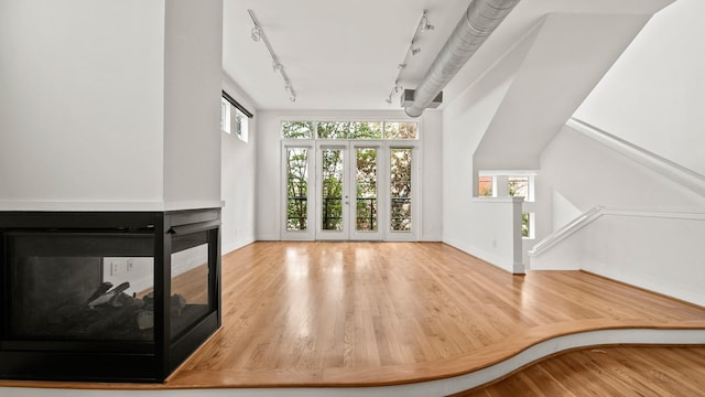 unfurnished living room with a multi sided fireplace, hardwood / wood-style floors, rail lighting, and plenty of natural light