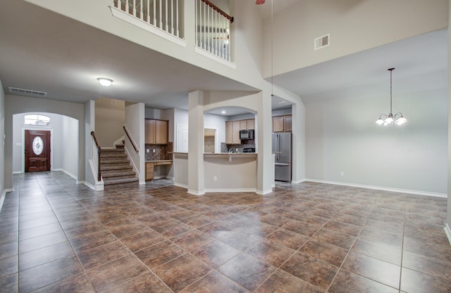 unfurnished living room with arched walkways, an inviting chandelier, visible vents, and baseboards