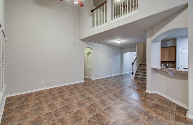 unfurnished living room with arched walkways, a ceiling fan, baseboards, stairs, and stone finish floor