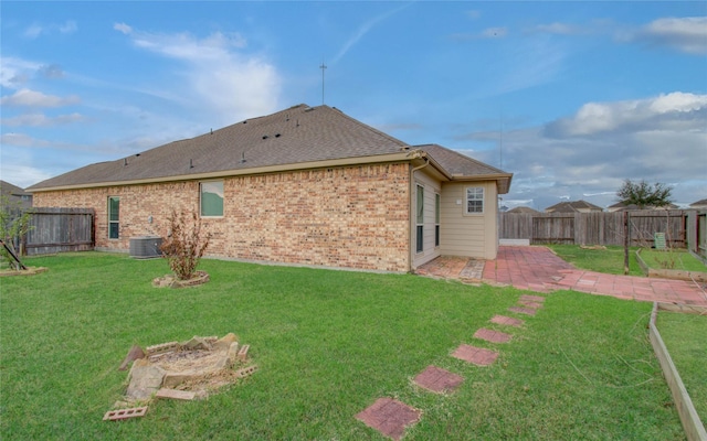 rear view of house with brick siding, a patio, a shingled roof, a lawn, and a fenced backyard