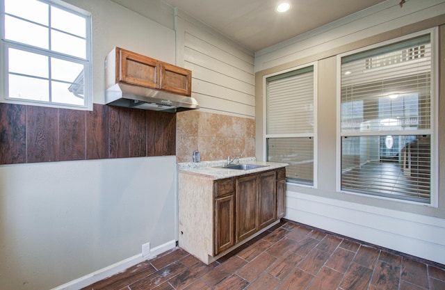 kitchen with under cabinet range hood, brown cabinetry, a sink, and wood finish floors