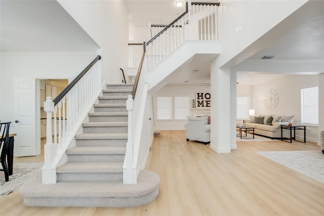 stairs featuring crown molding, a towering ceiling, and wood-type flooring