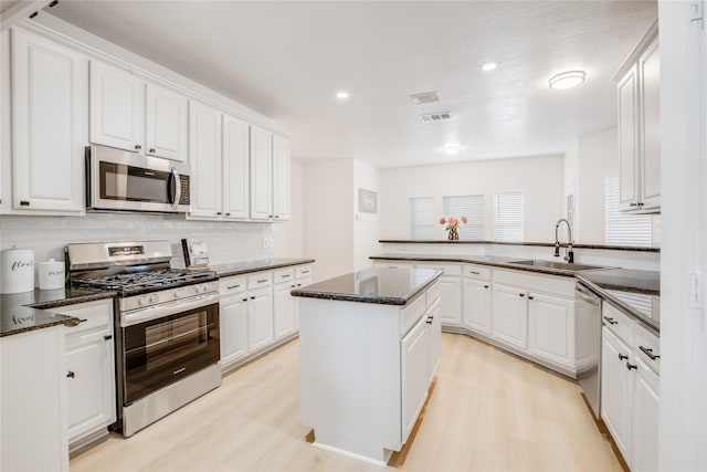 kitchen with sink, light wood-type flooring, a kitchen island, stainless steel appliances, and white cabinets