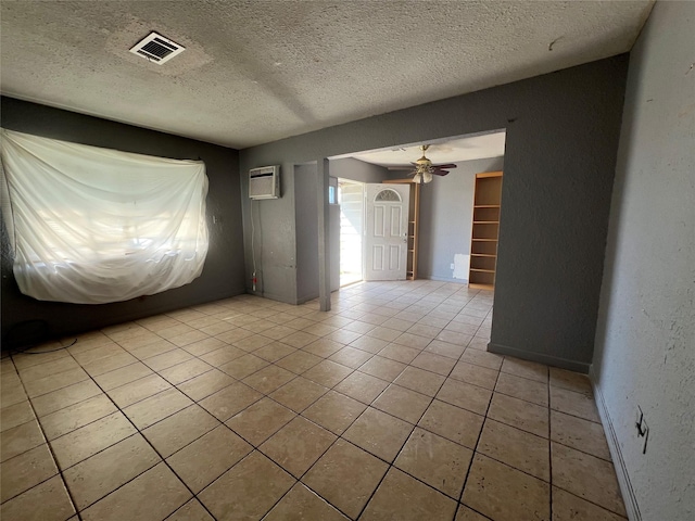 spare room featuring a textured ceiling, a wall mounted air conditioner, ceiling fan, and light tile patterned floors