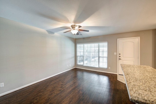 empty room featuring dark wood finished floors, a ceiling fan, and baseboards