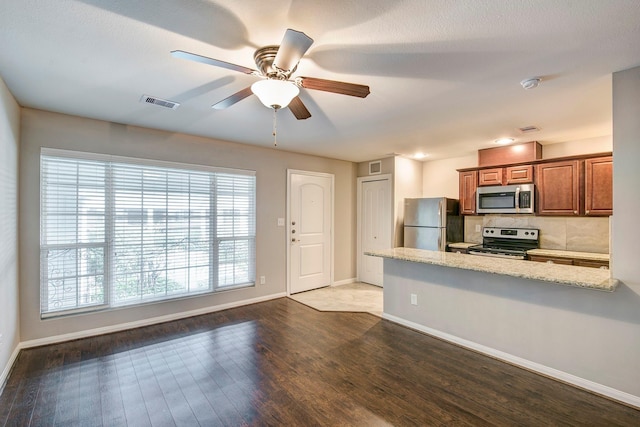 kitchen with appliances with stainless steel finishes, wood-type flooring, light stone counters, ceiling fan, and kitchen peninsula