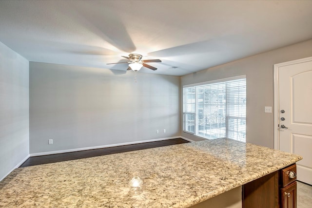 kitchen with baseboards, light stone counters, and a ceiling fan