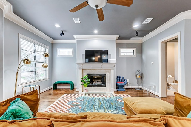 living room featuring a tiled fireplace, hardwood / wood-style flooring, crown molding, and ceiling fan