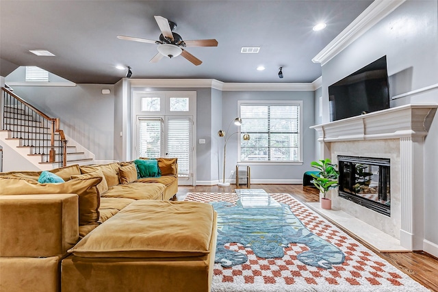 living room with ceiling fan, ornamental molding, a premium fireplace, and light hardwood / wood-style flooring