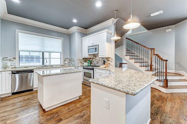 kitchen with appliances with stainless steel finishes, a kitchen island, white cabinetry, and decorative light fixtures