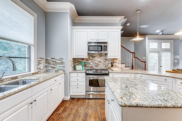 kitchen featuring hanging light fixtures, sink, light stone counters, wood-type flooring, and appliances with stainless steel finishes