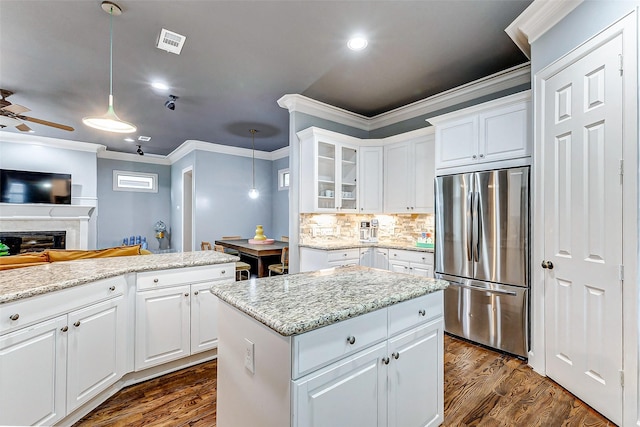 kitchen featuring white cabinetry, ornamental molding, stainless steel refrigerator, and hanging light fixtures