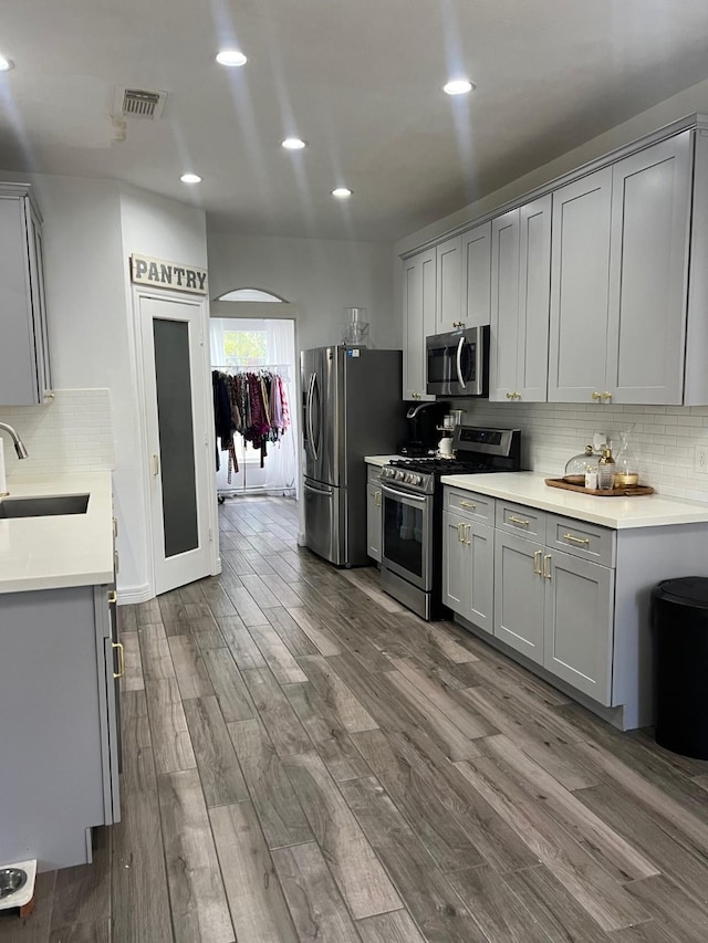 kitchen with gray cabinetry, dark wood-type flooring, stainless steel appliances, backsplash, and sink