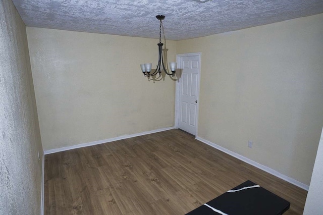 unfurnished dining area featuring a notable chandelier, a textured ceiling, and dark hardwood / wood-style floors