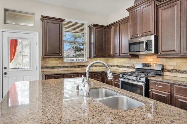 kitchen featuring sink, backsplash, appliances with stainless steel finishes, and light stone countertops