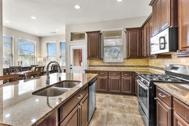 kitchen with appliances with stainless steel finishes, sink, stone counters, dark brown cabinets, and tasteful backsplash