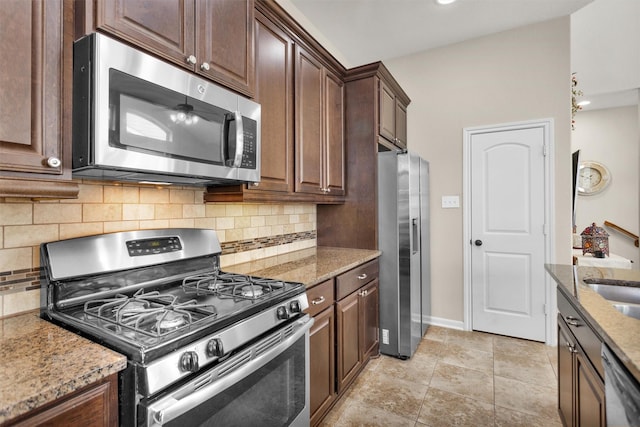 kitchen featuring stainless steel appliances, light stone countertops, sink, dark brown cabinets, and tasteful backsplash