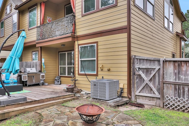 back of house featuring a balcony, a deck, central AC unit, and an outdoor living space with a fire pit