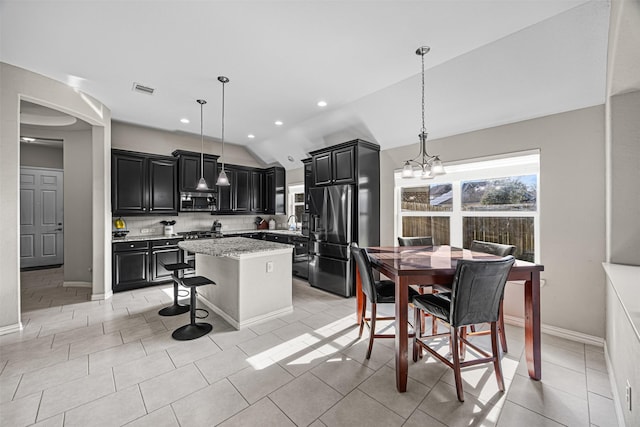 kitchen with appliances with stainless steel finishes, decorative light fixtures, a kitchen island, and dark cabinets