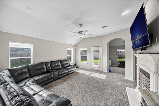 carpeted living area featuring baseboards, arched walkways, a ceiling fan, a fireplace with flush hearth, and vaulted ceiling