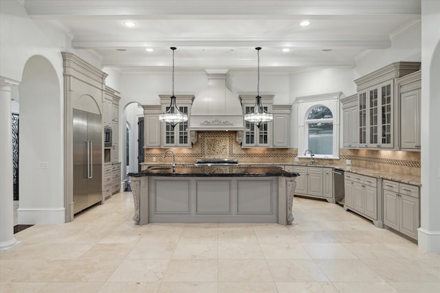 kitchen with decorative light fixtures, a kitchen island with sink, dark stone countertops, and premium range hood