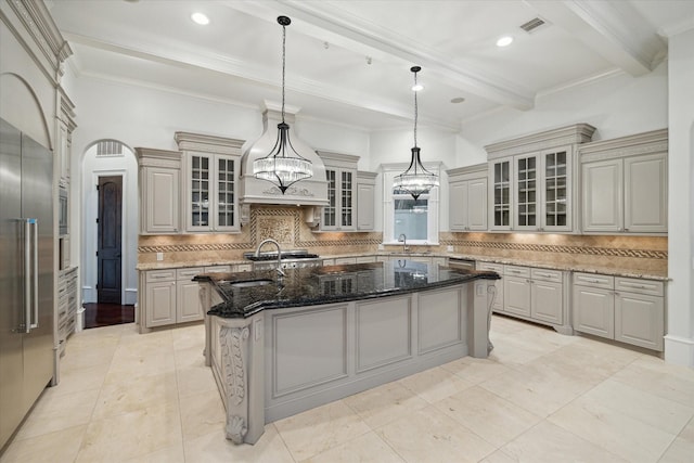 kitchen with hanging light fixtures, an island with sink, sink, and dark stone counters