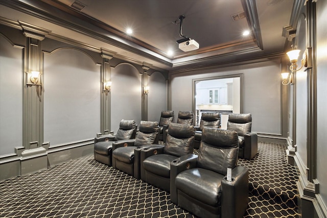 cinema room featuring a tray ceiling, crown molding, dark colored carpet, and decorative columns