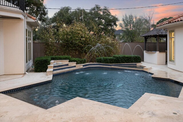 pool at dusk with a patio area, a gazebo, and pool water feature