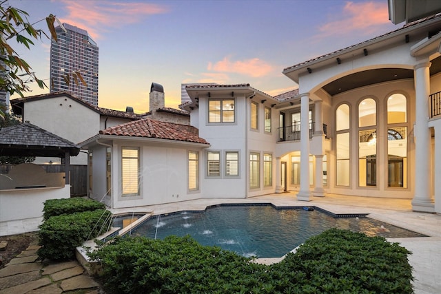 back house at dusk with pool water feature, a patio area, exterior kitchen, and a gazebo