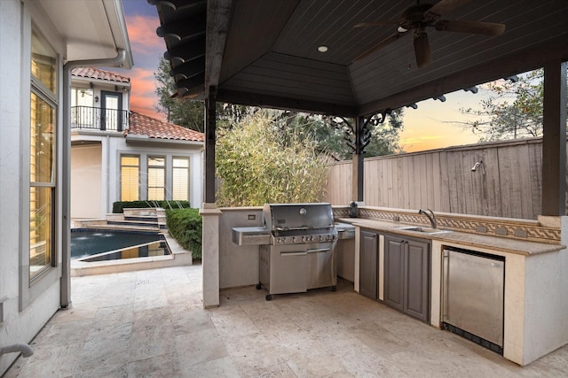 patio terrace at dusk featuring sink, a grill, a pool, exterior kitchen, and ceiling fan