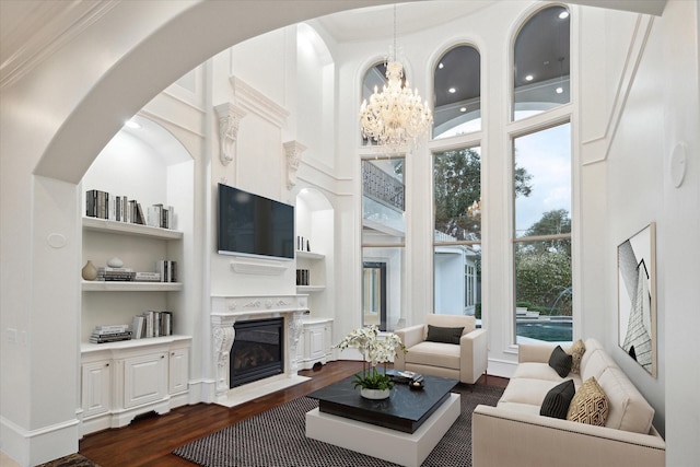 living room featuring a chandelier, a premium fireplace, built in shelves, a towering ceiling, and dark hardwood / wood-style flooring