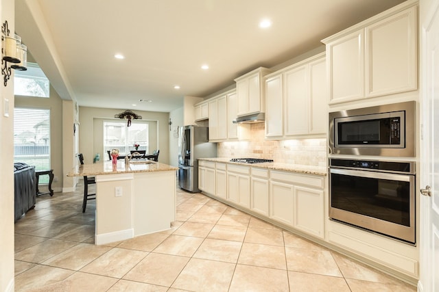 kitchen with appliances with stainless steel finishes, a center island with sink, a kitchen breakfast bar, light stone counters, and decorative backsplash