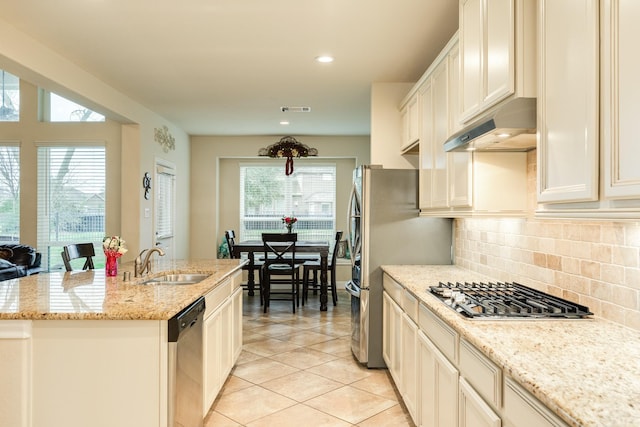 kitchen with a center island with sink, appliances with stainless steel finishes, tasteful backsplash, light stone countertops, and sink