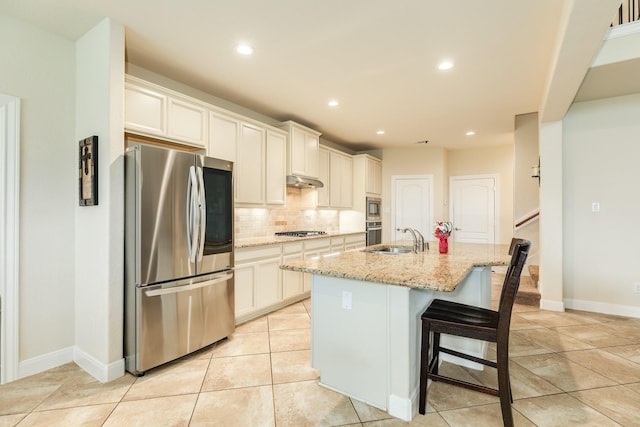 kitchen with a kitchen bar, sink, light stone counters, stainless steel appliances, and an island with sink