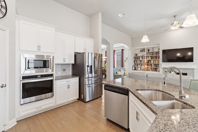 kitchen featuring white cabinetry, stainless steel appliances, hanging light fixtures, light stone countertops, and sink