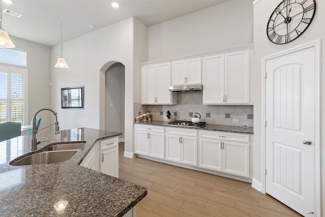 kitchen with stainless steel gas stovetop, hanging light fixtures, sink, dark stone counters, and white cabinets