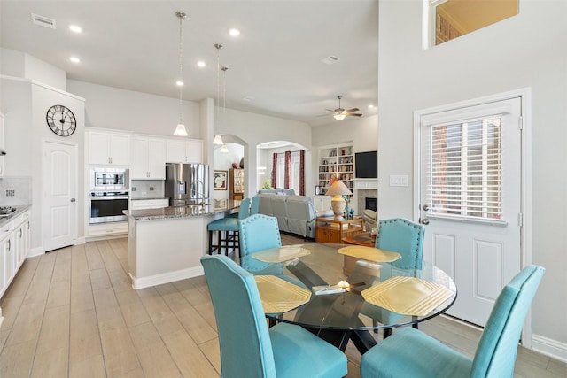 dining space featuring light hardwood / wood-style floors, ceiling fan, and a towering ceiling