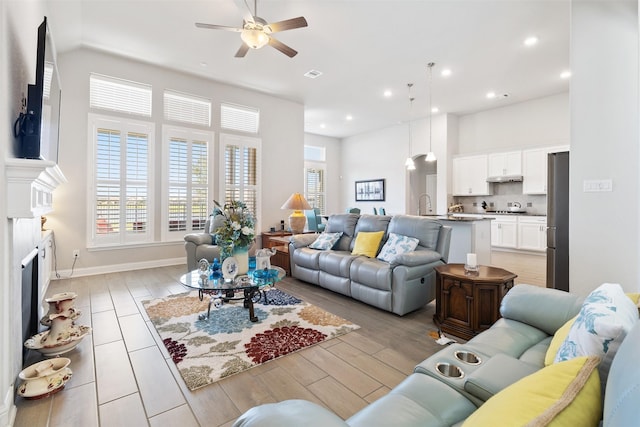 living room with ceiling fan, sink, a towering ceiling, and light hardwood / wood-style flooring