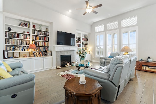 living room with ceiling fan, light wood-type flooring, built in features, and a tiled fireplace