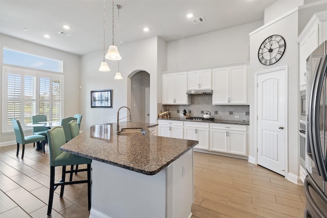 kitchen with hanging light fixtures, a kitchen breakfast bar, white cabinets, sink, and a kitchen island with sink