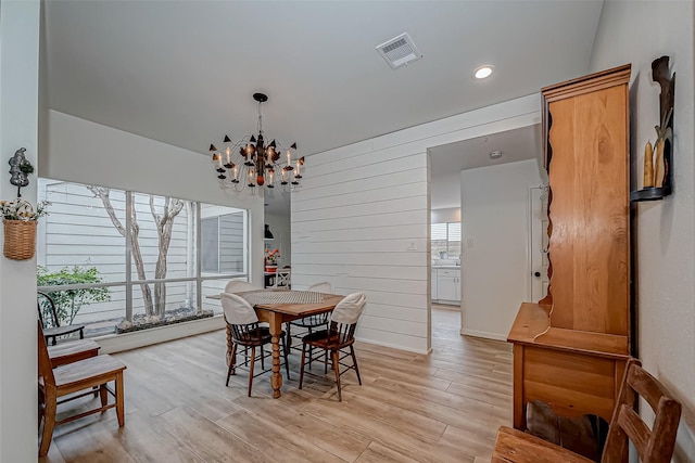 dining area featuring light wood-type flooring, wooden walls, and a notable chandelier