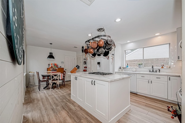 kitchen featuring light wood-type flooring, a kitchen island, sink, white cabinets, and pendant lighting