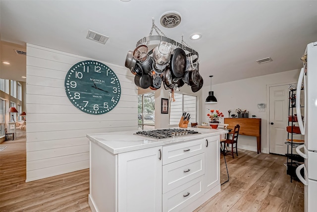 kitchen featuring stainless steel gas cooktop, pendant lighting, a kitchen island, light wood-type flooring, and white cabinetry