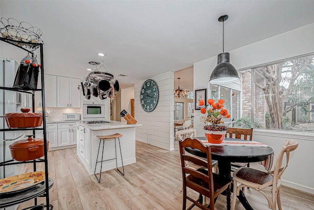 kitchen with a wealth of natural light, light wood-type flooring, hanging light fixtures, and white cabinets