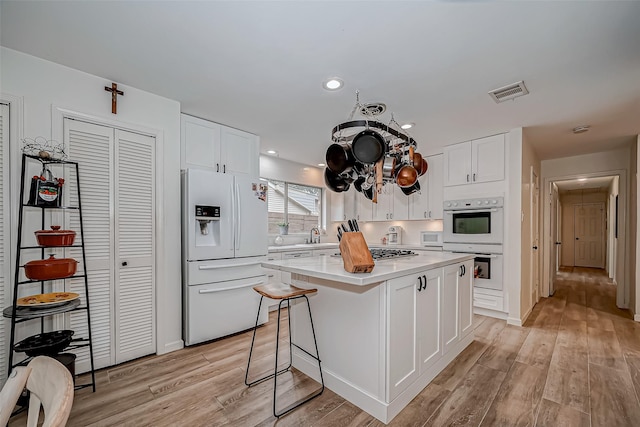 kitchen featuring white appliances, an inviting chandelier, a center island, light wood-type flooring, and white cabinets