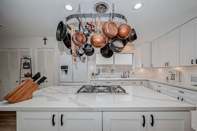 kitchen featuring white refrigerator with ice dispenser, sink, white cabinetry, and light stone countertops