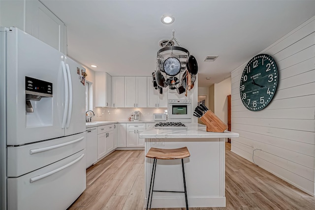 kitchen with white appliances, a breakfast bar, white cabinets, and light hardwood / wood-style floors